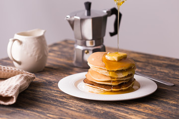 Maple syrup pouring over a stack of mini pancakes.