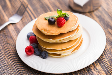 Pile of pancakes with blueberries and raspberries for breakfast on wooden table.