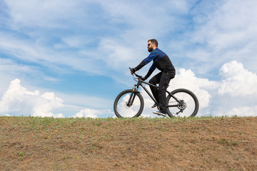 Fototapeta na wymiar Bearded mountain bicyclist rides mountains against the beautiful sky