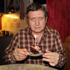 Portrait of a happy elderly man smiling at the camera, sitting at a table with a cake, about to blow out a candle and make a wish.