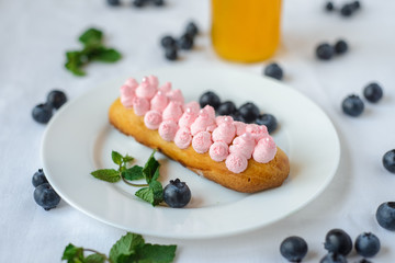 Tasty homemade eclairs on a white tablecloth. Blueberries are scattered everywhere.