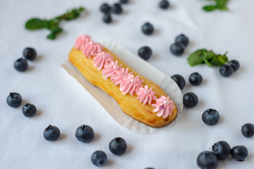 Tasty homemade eclairs on a white tablecloth. Blueberries are scattered everywhere.