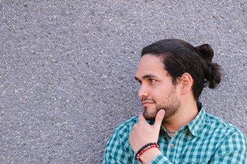 Junger Mann mit schwarzen langen Haaren posiert vor grauem Hintergrund