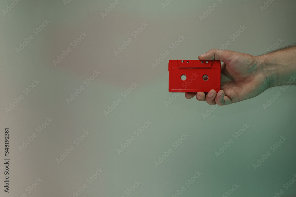 Poster Hand holding red audio cassette tape in the color light. Beautiful minimal in neon light. Minimalism retro style concept. Background pattern for design.
