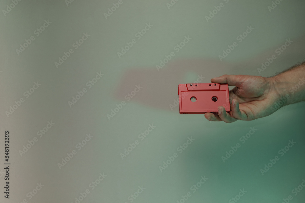 Poster Hand holding red audio cassette tape in the color light. Beautiful minimal in neon light. Minimalism retro style concept. Background pattern for design.