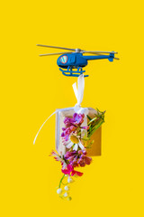 Yellow paper box gift toy delivery helicopter yellow background fly flowers
