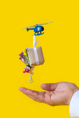 Yellow paper box gift toy delivery helicopter hand background flowers