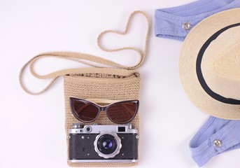 Fashion woman stylish traveling accessories flat lay: denim dress, camera, small bag, sun glasses and straw hat on white background. Tourist travel or vacation concept.Top view