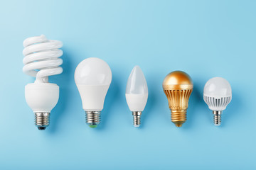 One Golden light bulb in a row of energy-saving white lamps on a blue background.