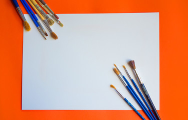White sheet of paper on a red background. Paints and brushes on the table. Creation. Drawing with...