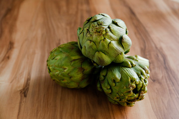 Fototapeta premium Fresh green Italian Artichoke natural wood background. Organic local produce vegetable on textured table. Vegan diet. Clean eating concept. Close up, top view, flat lay.