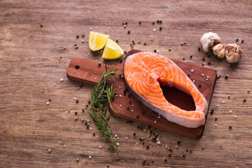 Raw steak of salmon with fresh lemon and rosemary and pepper on the wooden board top view. Healthy food and diet concept.
