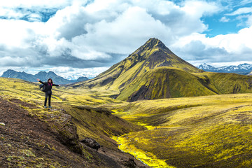 A young woman on a green mountain and a beautiful river of moss on the 54 km trek from Landmannalaugar, Iceland - obrazy, fototapety, plakaty