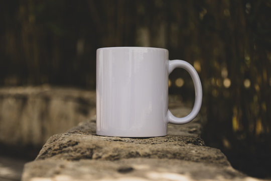 White Coffe mug with no design outside over the rocks with the blured background, perfect for business. Can be used for muck-ups and used your design