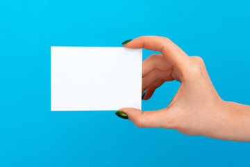 Woman hand holding blank card on blue background, close up.