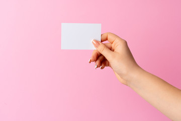 Woman hand showing blank business card on pink background. Close up.