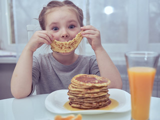 Funny little girl holds in front of the face a piece of pancake in the form of a smile.