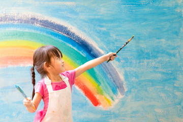 Asian little girl is painting the colorful rainbow and sky on the wall and she look happy and...