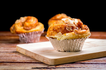 Delicious homemade almond danish bread in foil cup on a wooden table in the home kitchen on black background.