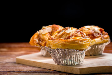 Delicious homemade almond danish bread in foil cup on a wooden table in the home kitchen on black background.