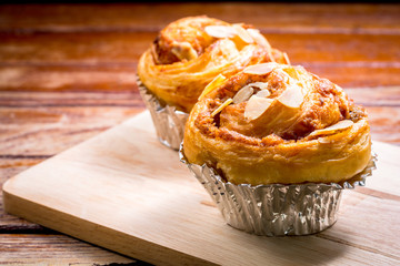Delicious homemade almond danish bread in foil cup on a wooden table in the home kitchen on black background.