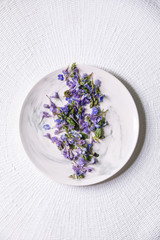 Violet purple edible flowers on white plate over white textile background. Flat lay, space