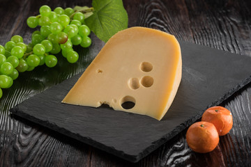 A slice of Maasdam cheese on a slate boars with a grape