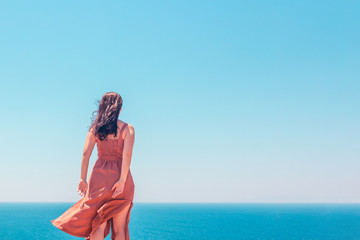 Young girl in brown summer dress looking at the sea getting ready to dive into it in clothes, long-awaited vacation concept, horizontal copy space