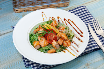 Rice noodles with salmon and spinach. Lunch in a white plate on the table. Tomatoes, lemon, fish, rosemary, soi and sesame seeds. Food still life. Fork Spoon Knife.