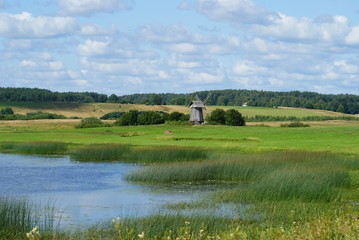 Obraz premium old mill on a green meadow against the next to the pond river lake