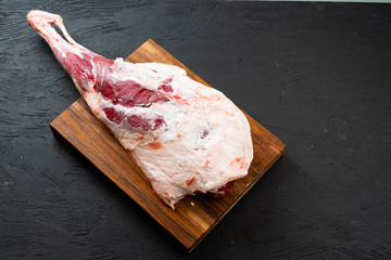 Fresh raw lamb leg ready for roasting on wooden board, top view.