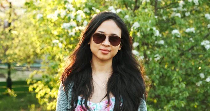 Cool fashionable asian girl walks in green fresh park at sunset. Confident woman