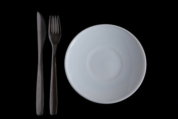 A metal knife, fork, and white plate on a black background. Suitable for mockups