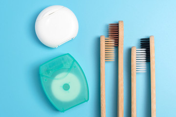 Dental floss containers and bamboo toothbrushes on blue background. Daily oral hygiene, teeth care and health. Cleaning products for mouth. Dental care concept. Empty place for text or logo