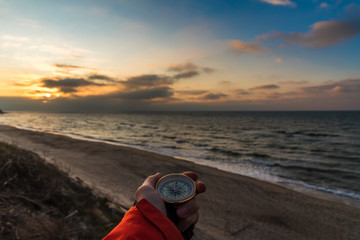 First-person view of a female hand with a compass on a background of a beautiful sea landscape. The concept of navigating the search for your own path and orientation to the cardinal points
