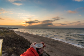 First-person view of a female hand with a compass on a background of a beautiful sea landscape. The concept of navigating the search for your own path and orientation to the cardinal points