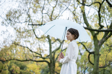 雨の公園で傘をさして佇む白いワンピースを着た若い女性