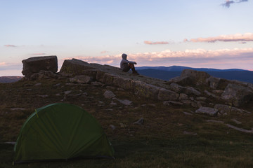 Man watching a sunset in the mountains with a green tent.