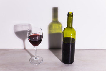 A glass of wine and a bottle casts a long shadow from the evening sun.