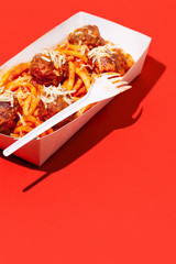 Italian spaghetti and meatballs with tomato sauce in takeaway packaging box on red background with shadow.Restaurant food delivery concept