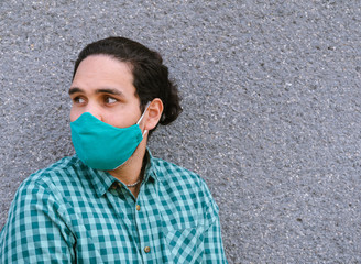 Mann mit schwarzen Haaren trägt Schutzmaske vor grauem Hintergrund, COVID-19, Coronavirus
