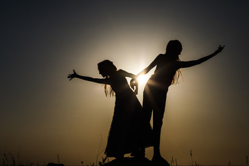 Two sisters are standing next to each other. Silhouettes.