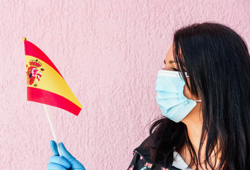 Woman with Surgical Face Masks holds flag of Spain . Coronavirus Epidemic or Pandemic concept for travel, Tourism or something similar