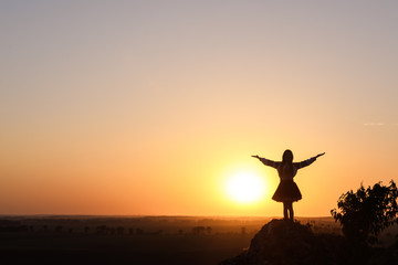 Fototapeta premium Silhouette of a girl standing on a rock and spreads her arms.