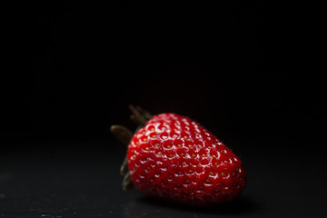 A close up macro photograph of a whole fresh ripe organic strawberry on a dark black slate stone background with copy space.