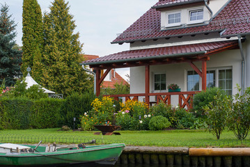 Beautiful white house with red roof on the river bank. In front of it there is a green lawn and a...