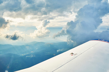 Fototapeta na wymiar Aerial photo of a small plane wing and beautiful clouds in the sky and silhouettes of hills and meadows