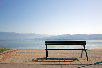 Fototapeta na wymiar A bench silhouette overlooks the mountains surrounding Dojran Lake. Atmospheric Perspective.