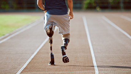 Athletic Disabled Fit Man with Prosthetic Running Blades is Training on Outdoors Stadium on Sunny Afternoon. Amputee Runner Jogging on a Stadium Track. Motivational Sports Shot. Leg Shot.