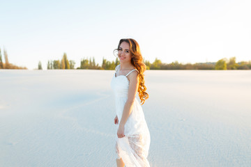 Fototapeta na wymiar Attractive girl in a white dress walks on the sand in a white desert